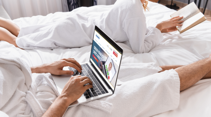 A man comfortably sits in bed and visits the Boston Medical Group Telemedicine website on his laptop.