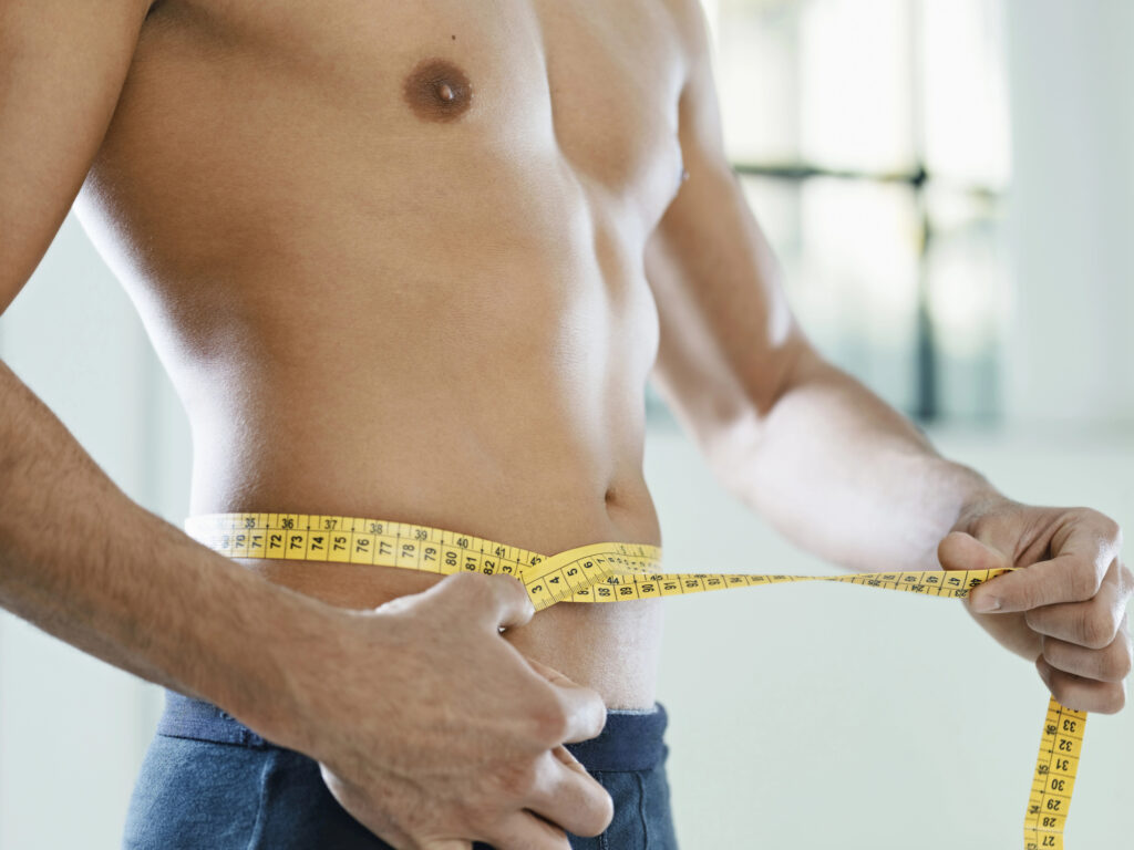 A man measuring his waist using a measuring tape, illustrating the effectiveness of weight loss injections for men in achieving fitness goals.